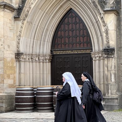 Nonnen vor der Marienkirche, den Eingang mit Bierfässern zugestellt ist.