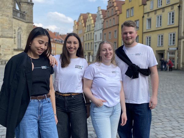 Vier Personen mit T-Shirt, Sweatshirt, Tennissocken und Cap aus der Merchandising-Kollektion mit dem frisch eingeführten Stadtlogo.